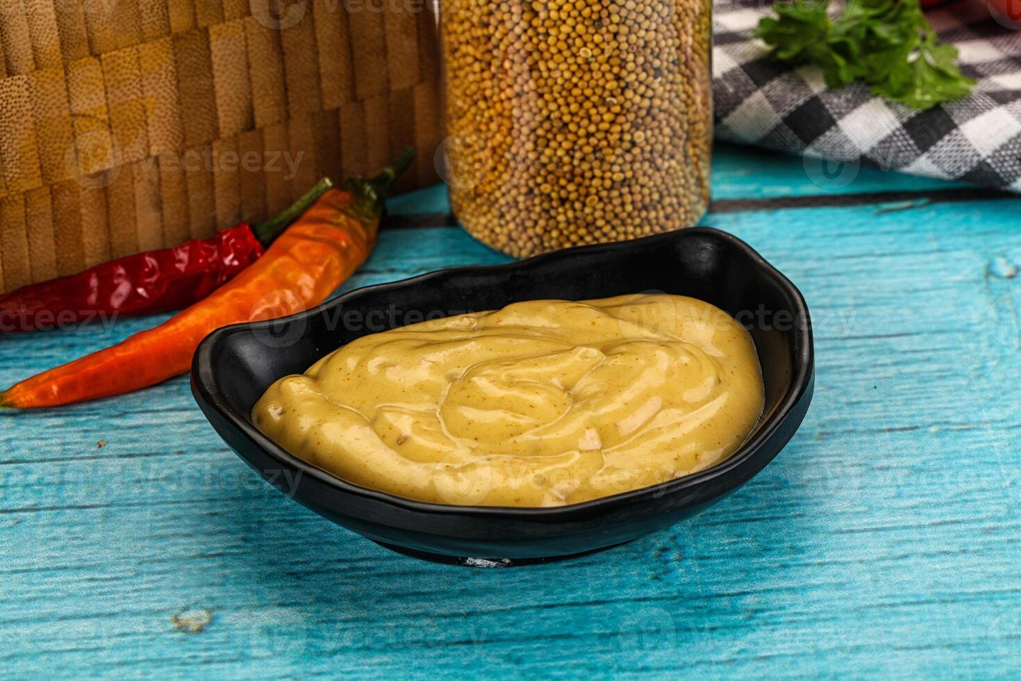 A bowl of mustard and a bottle of mustard on a wooden table photo