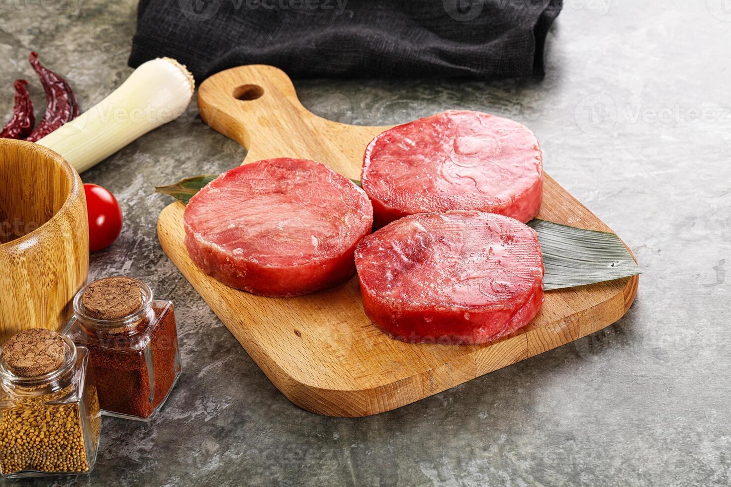 Three raw beef steaks on a cutting board with spices and other ingredients photo