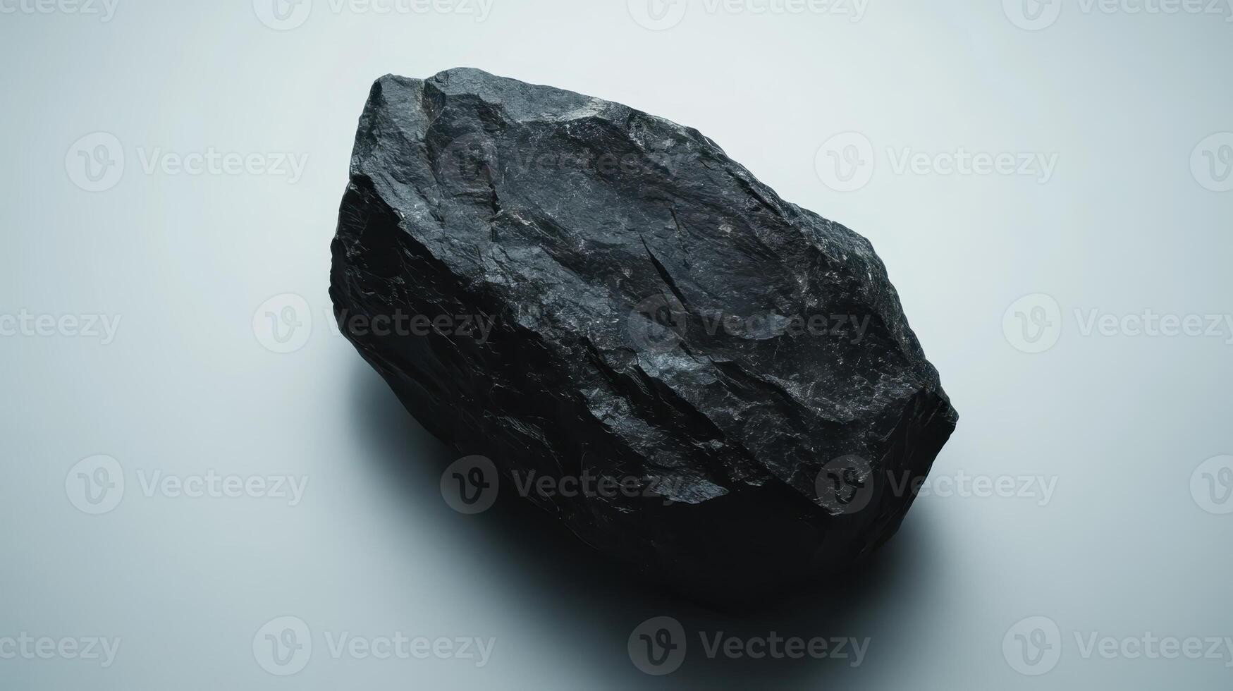 Large black rock displayed on a light background showcases texture and surface detail under soft lighting conditions photo