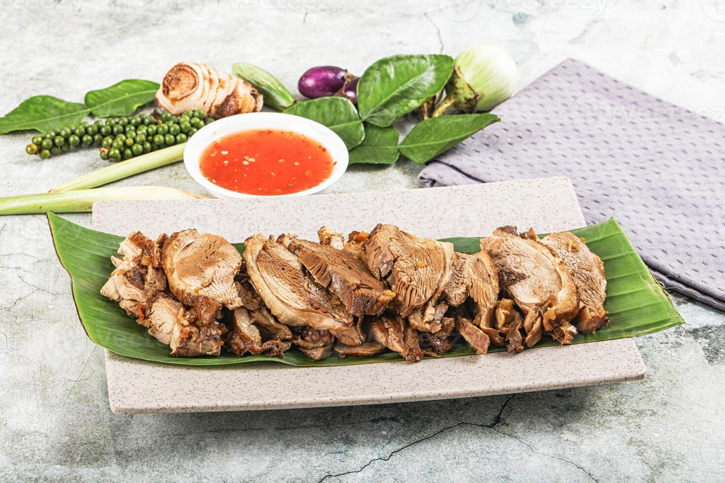 A plate of meat on a leaf with a bowl of sauce photo