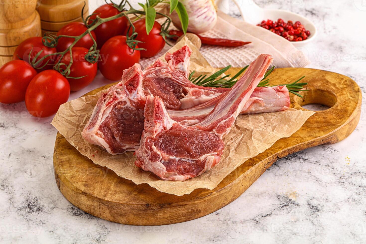 Raw lamb chops on a cutting board with tomatoes and herbs photo