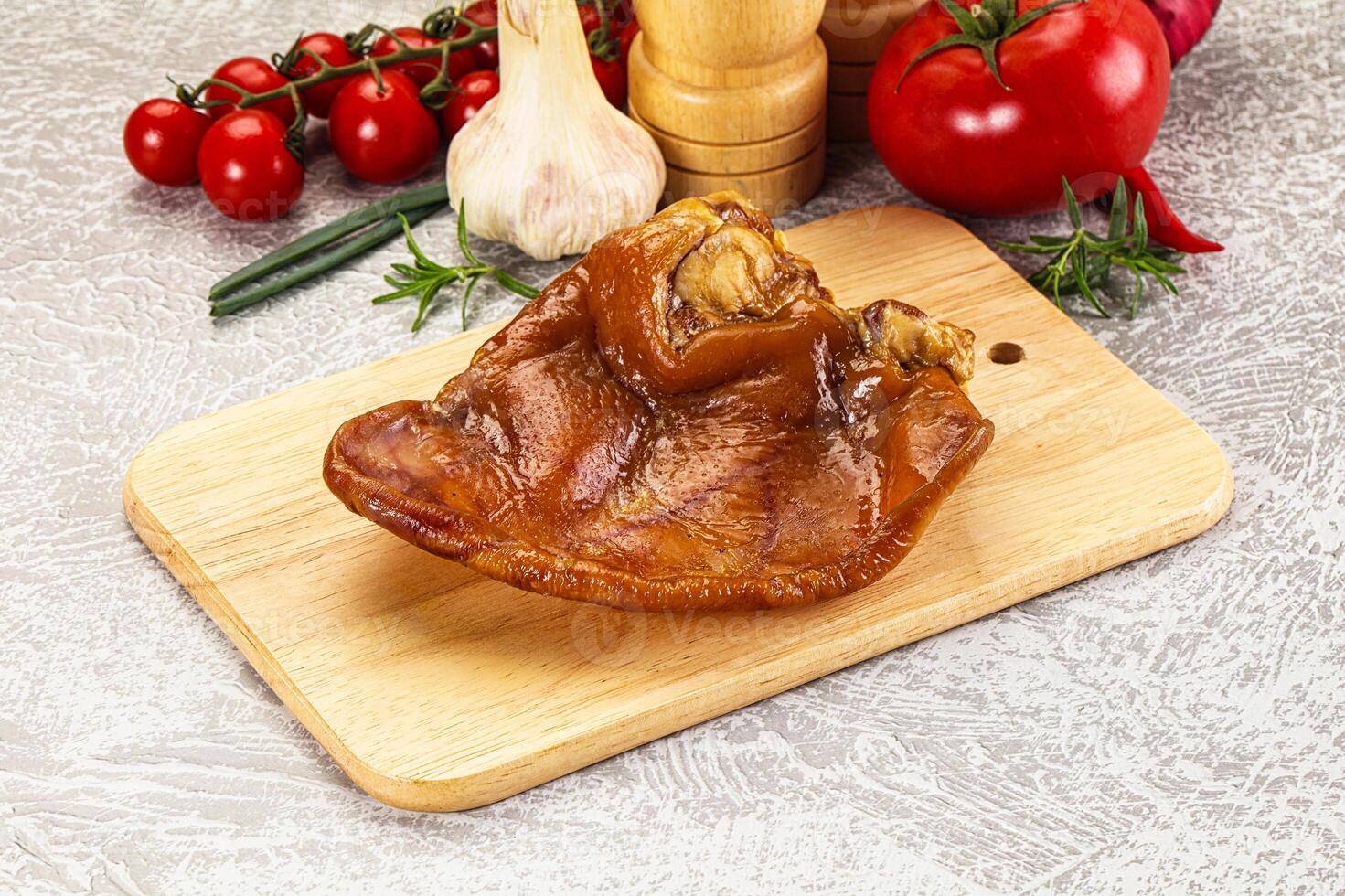 A piece of meat on a cutting board with tomatoes and garlic photo