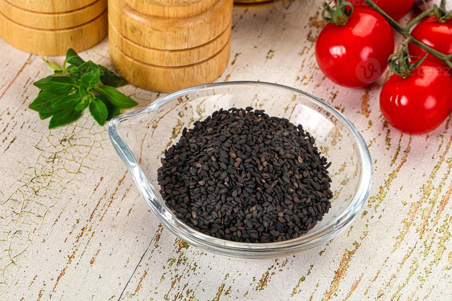A bowl of black seeds and tomatoes on a wooden table photo