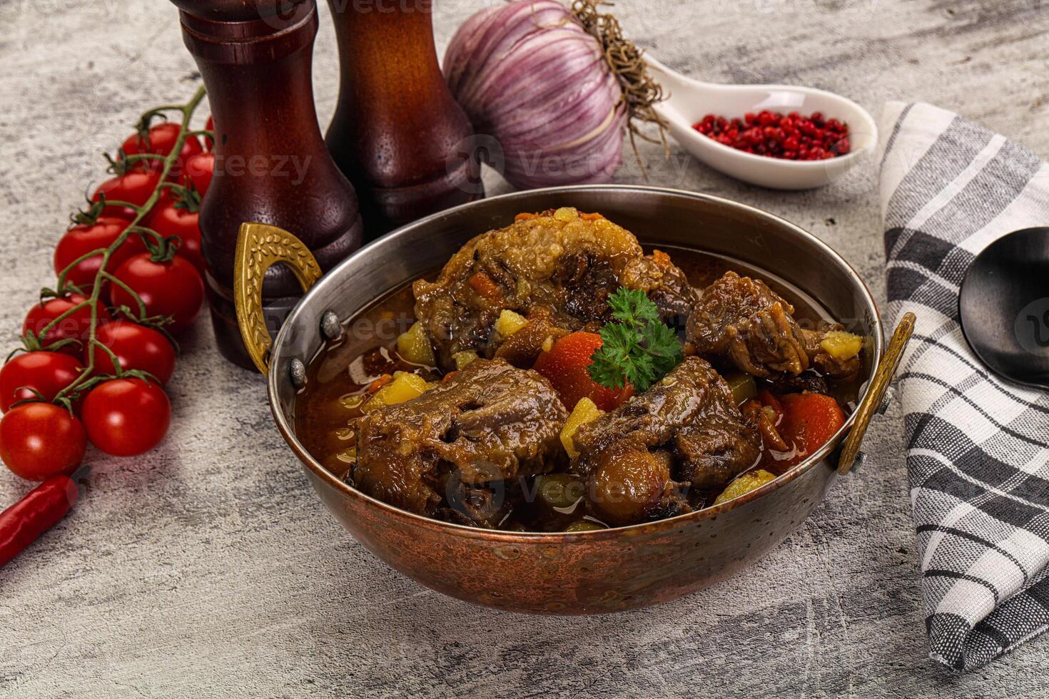A bowl of stew with meat and vegetables on a wooden table photo