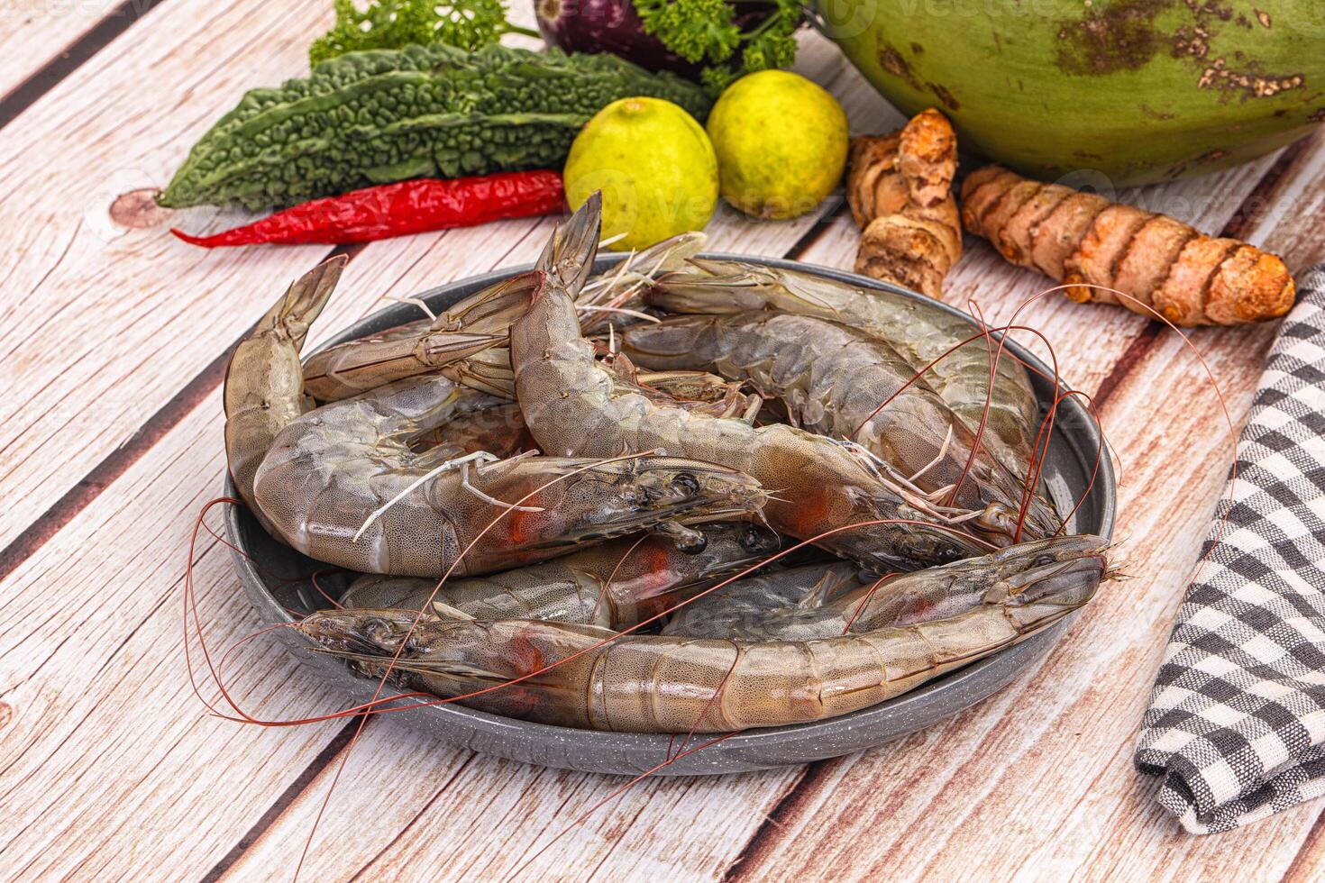 A bowl of shrimp on a table next to vegetables photo