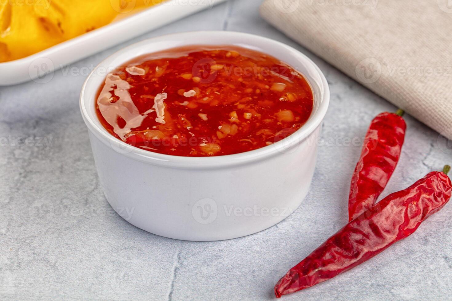 A bowl of chili sauce next to a bowl of chili peppers photo