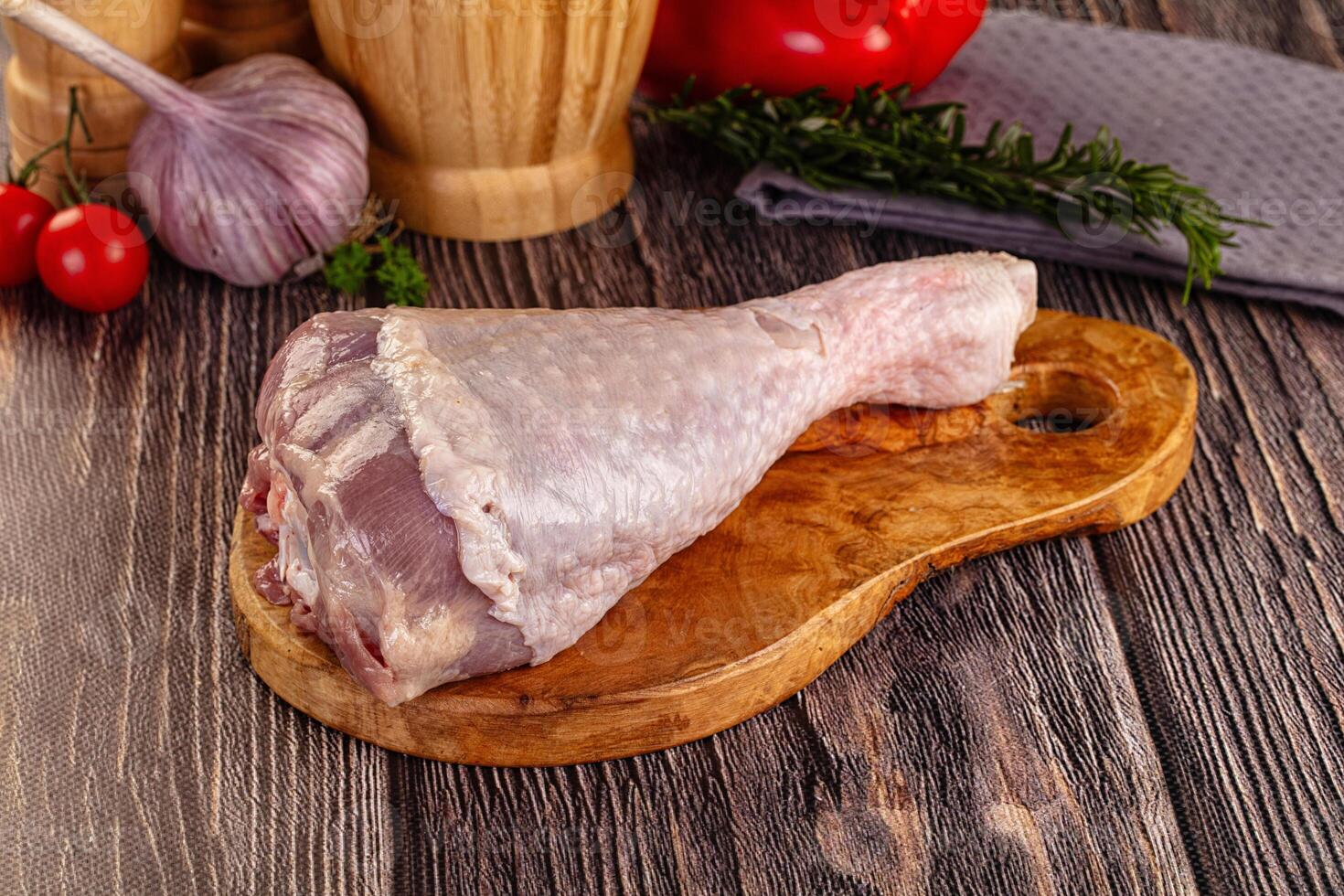 Raw chicken leg on wooden cutting board with vegetables and herbs photo
