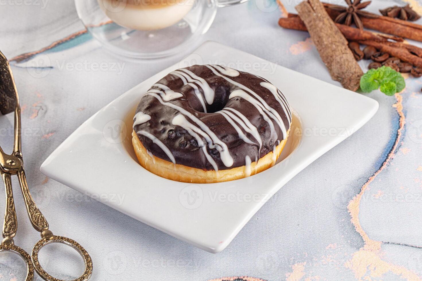 A chocolate donut on a white plate with a cup of coffee photo
