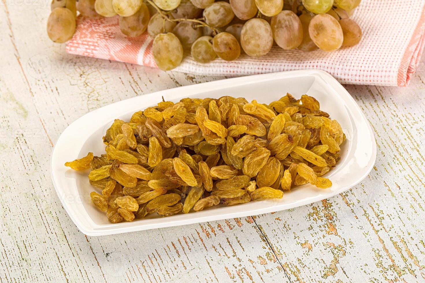A bowl of raisins and a bunch of grapes on a table photo