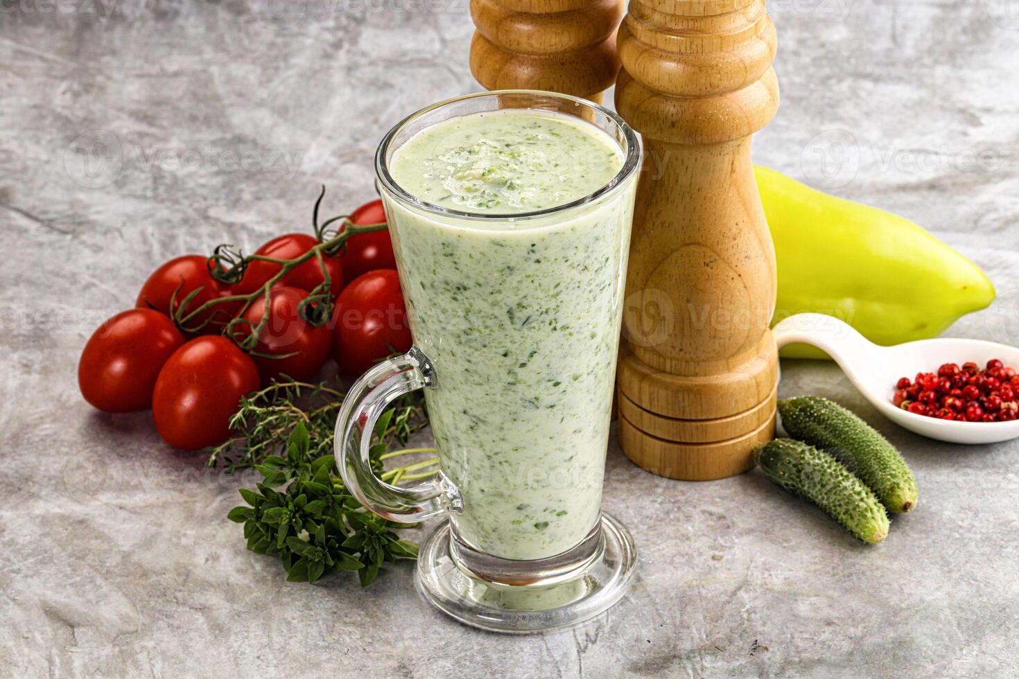A glass of green smoothie next to a pepper grinder photo