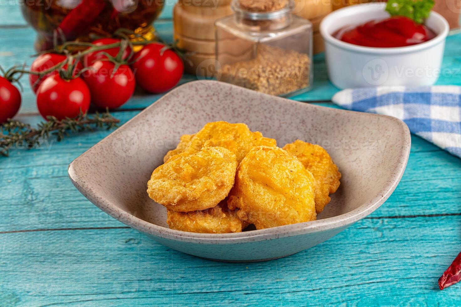 A bowl of fried food on a table next to a bottle of ketchup photo