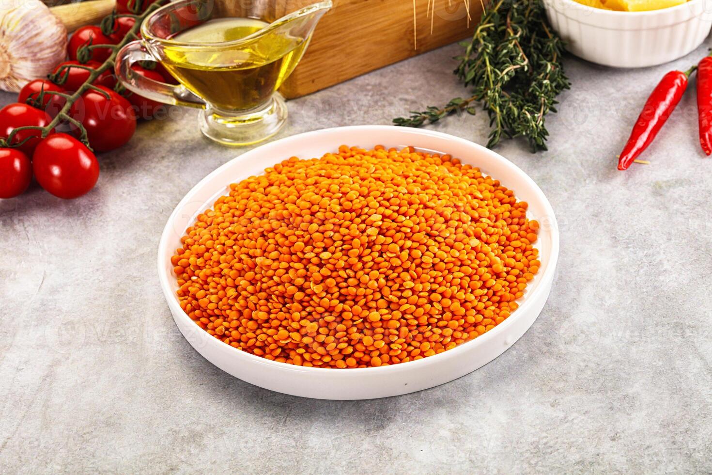 A bowl of red lentils sitting on a counter next to a bowl of tomatoes and garlic photo
