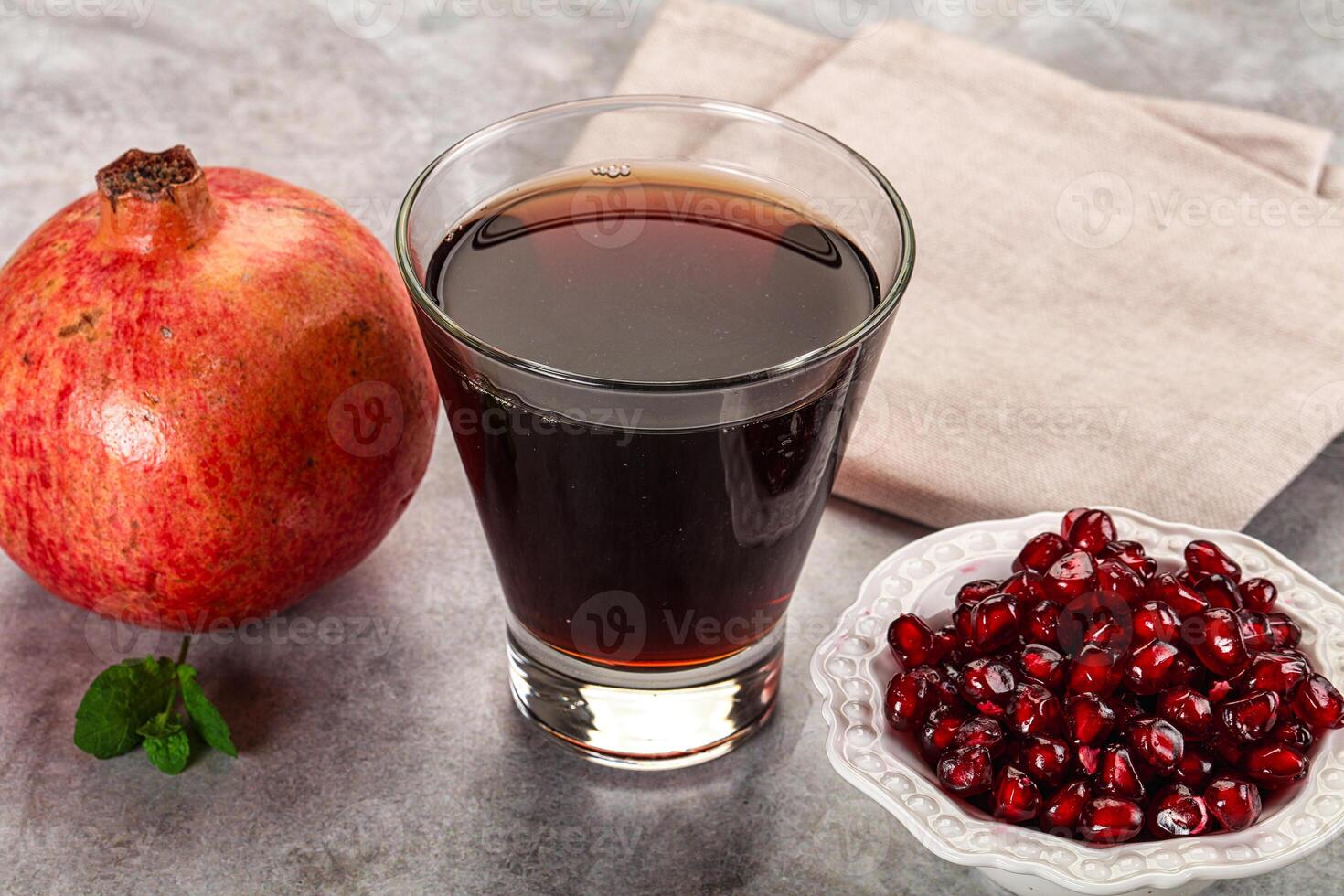 A glass of liquid next to a bowl of pomegranate photo