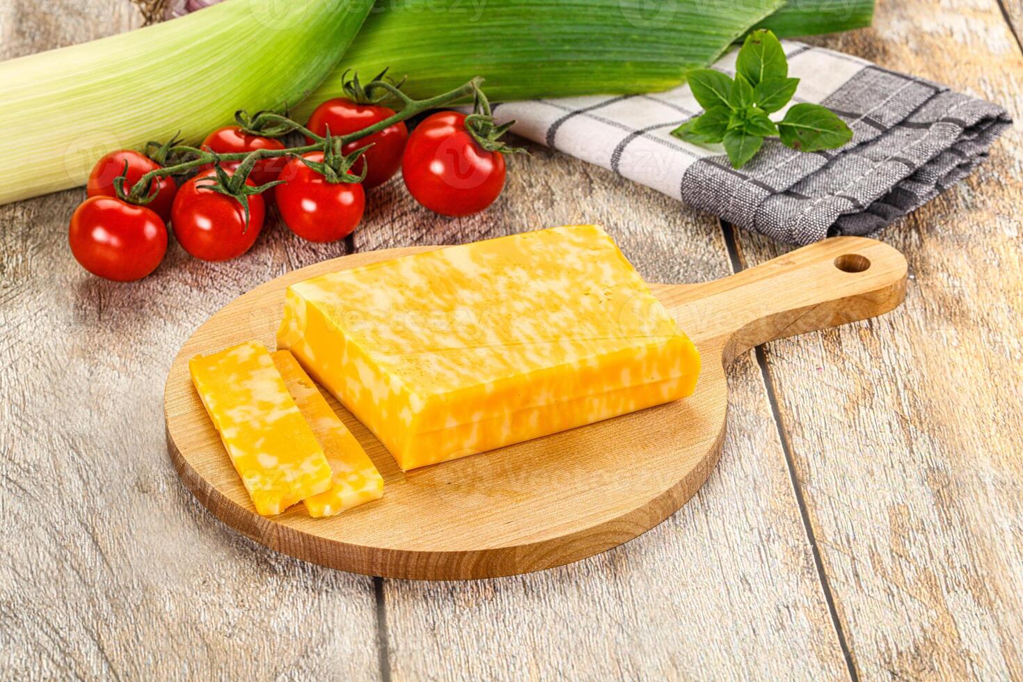 A wooden cutting board with cheese and vegetables photo
