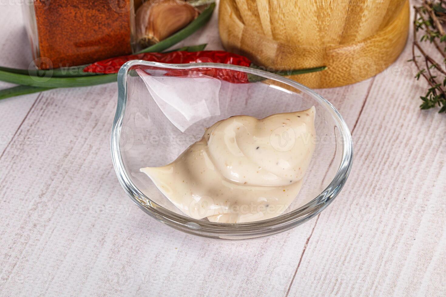 A bowl of dressing sitting on a table next to a bottle of sauce photo