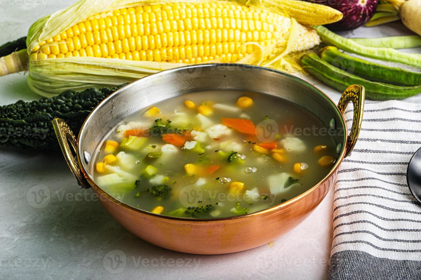 A bowl of vegetable soup with corn, carrots and other vegetables photo