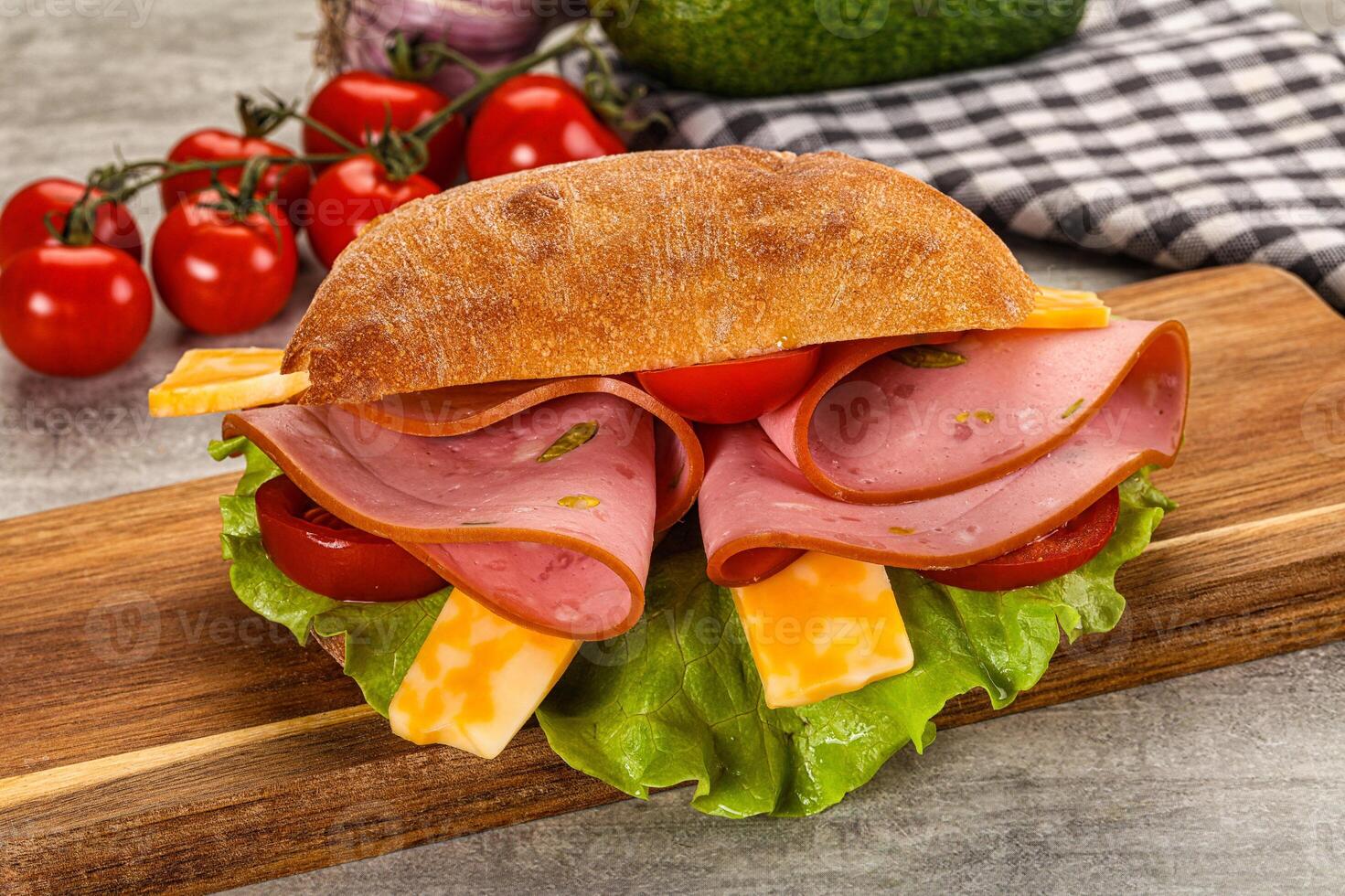 A sandwich with ham, cheese and tomatoes on a wooden cutting board photo