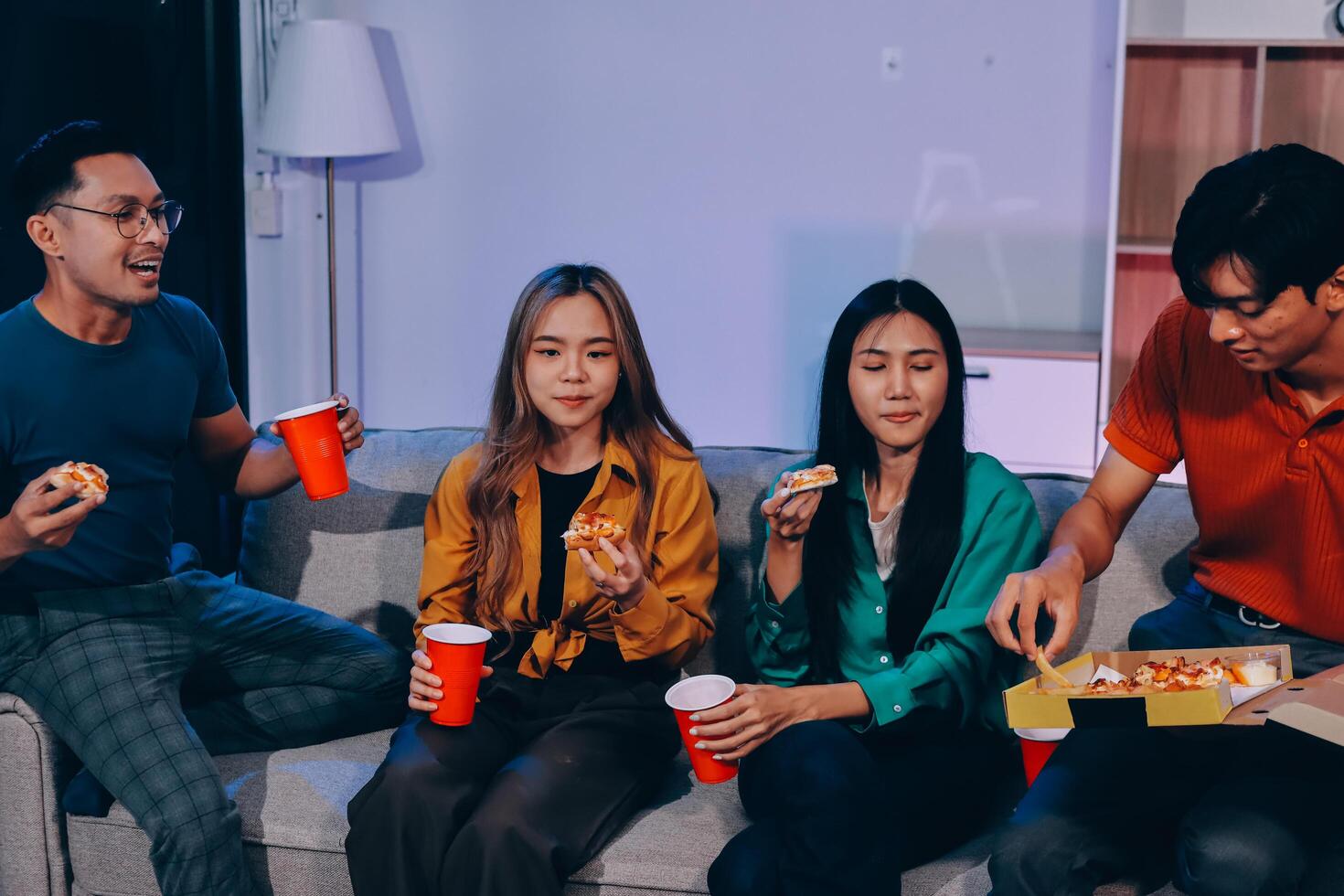 Four people sitting on a couch eating pizza photo