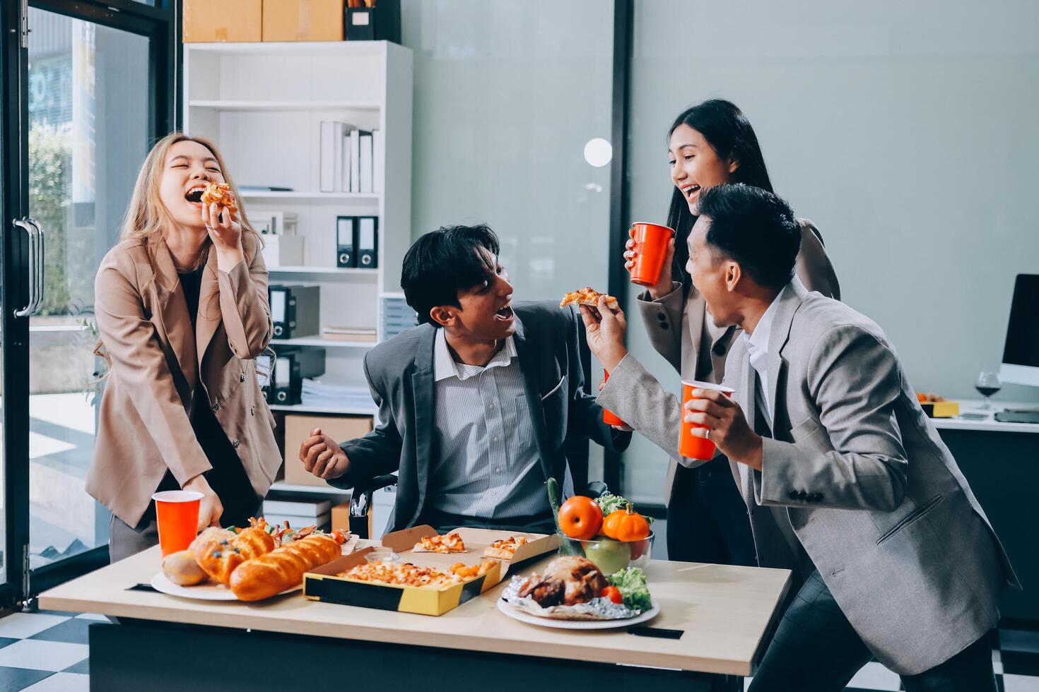 Happy asian business people eating pizza and drinking coffee in office photo