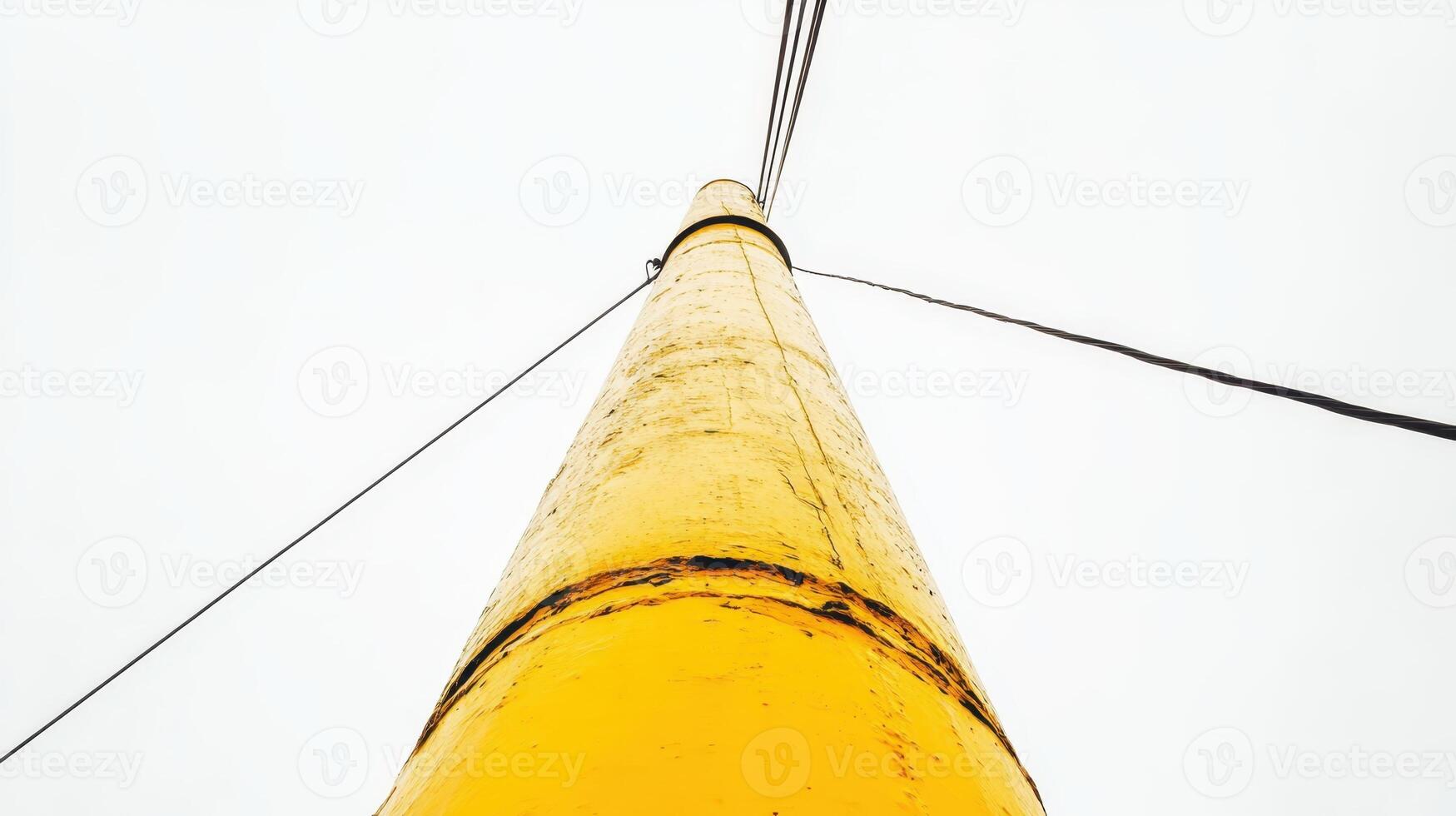 Yellow utility pole stretches into gray sky, capturing the tranquility of an overcast day in a rural area photo