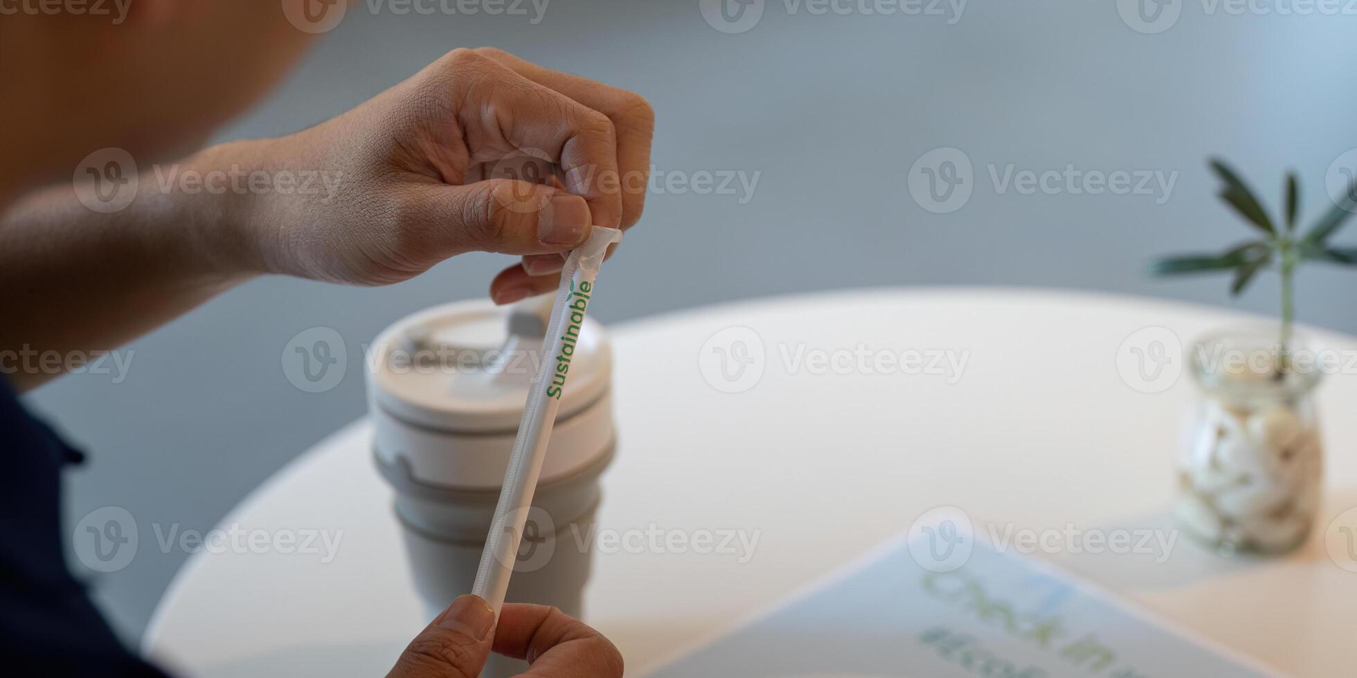 Sustainable and Responsible Choices. An individual holding a sustainable straw next to a reusable coffee cup on a table. photo