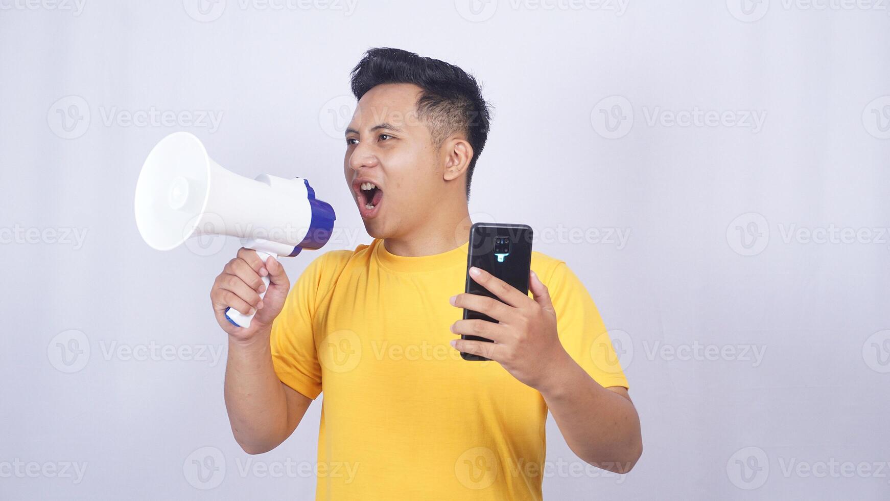 Frustrated Asian man holding mobile phone and shouting on megaphone isolated on white background photo