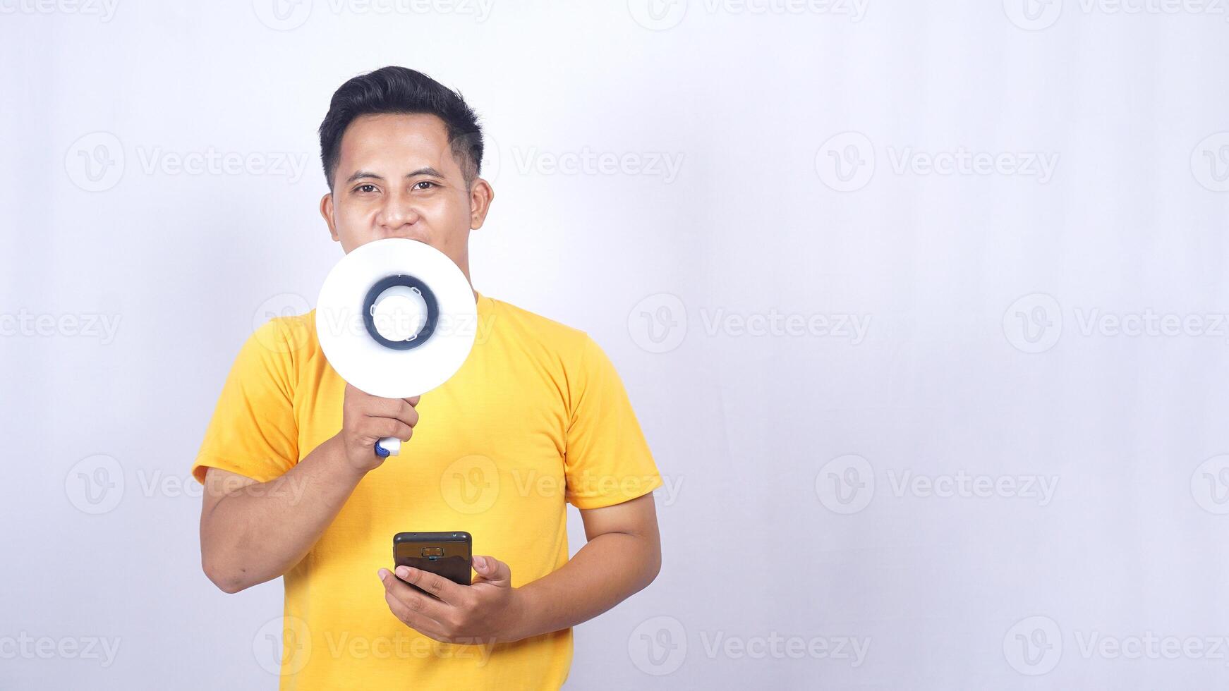 Portrait of Asian man holding mobile phone and shouting on megaphone isolated on white background photo