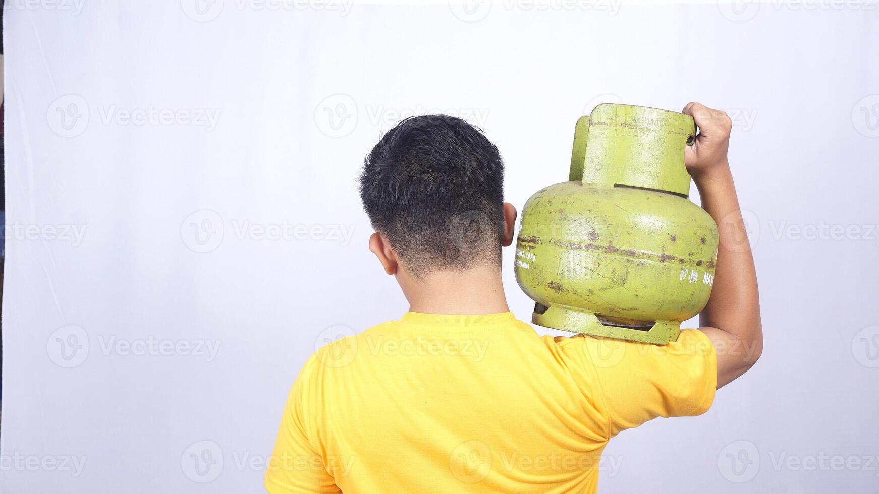 Rear view of Asian man carrying Indonesia 3kg green LPG gas cylinder on his shoulder isolated on white background photo