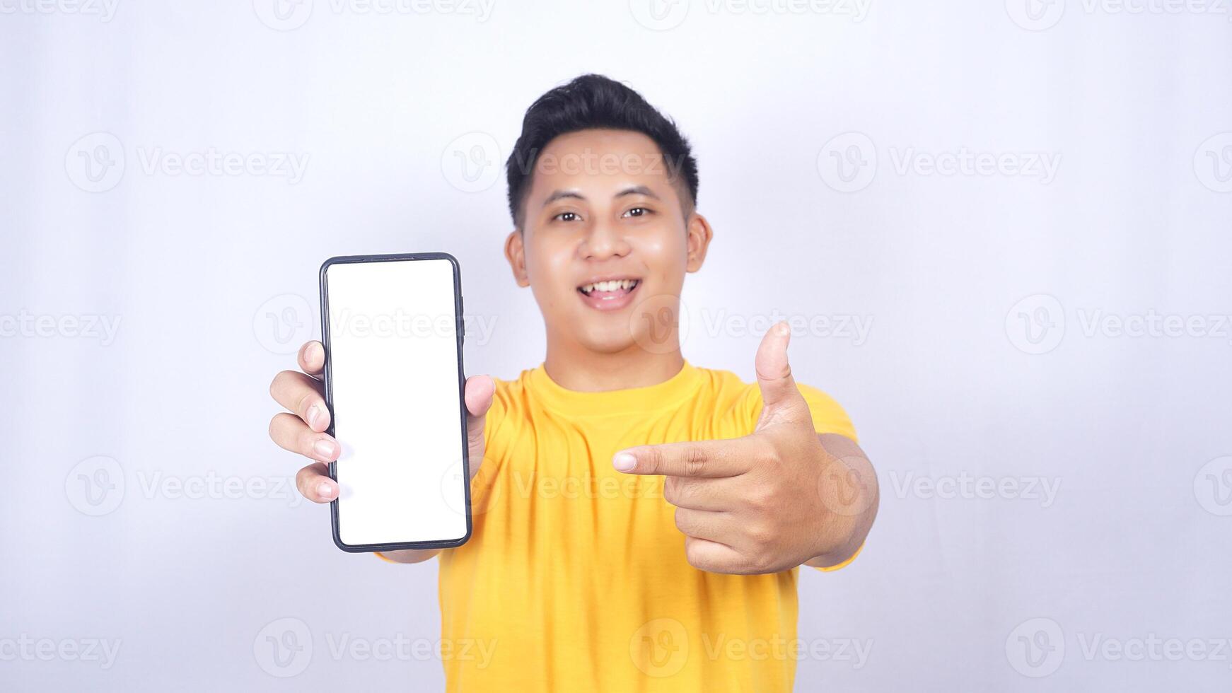 Happy Asian man showing mobile phone blank screen mock up and pointing at it isolated on white background photo