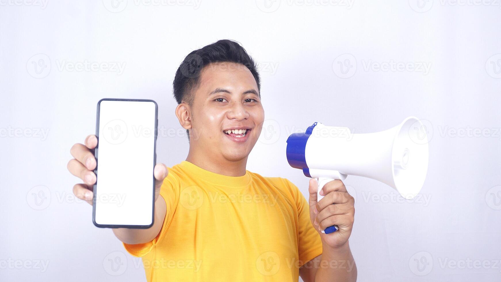 Smiling Asian man holding megaphone and showing mobile phone blank screen mock up isolated on white background photo