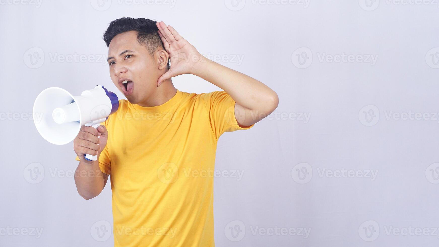 Asian man shouting on megaphone and placing his hand open behind his ear isolated on white background photo