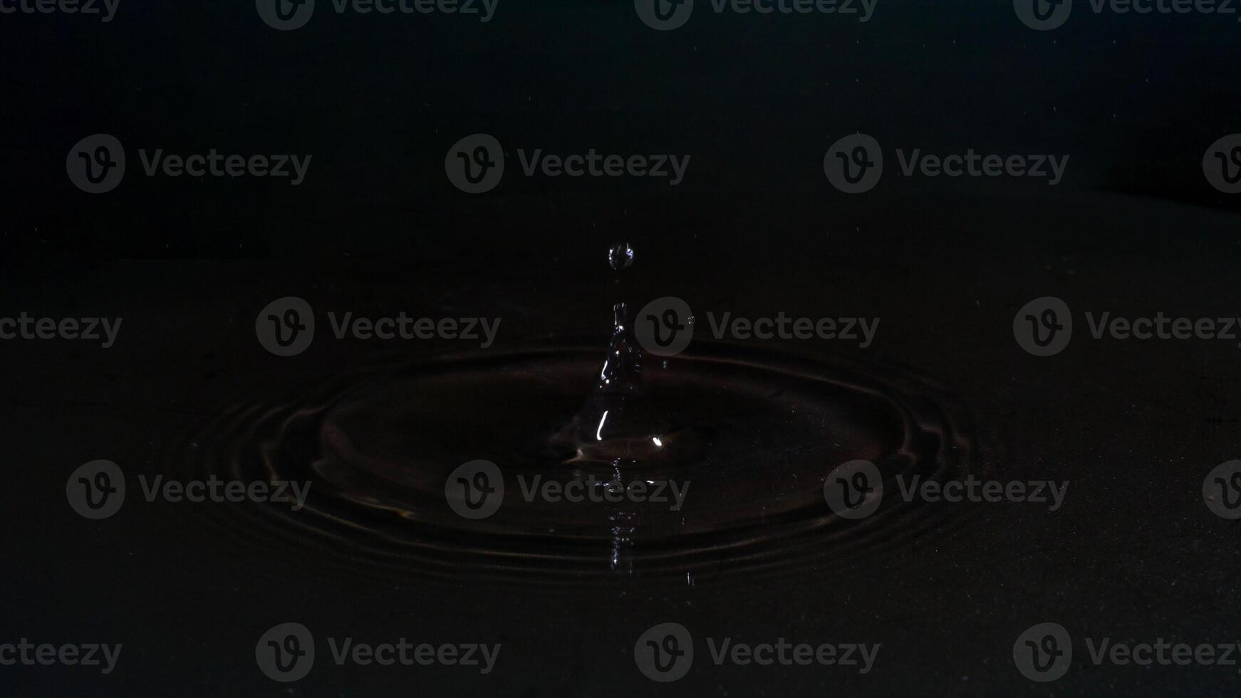 Drop falling down to water and splashing isolated on black background photo