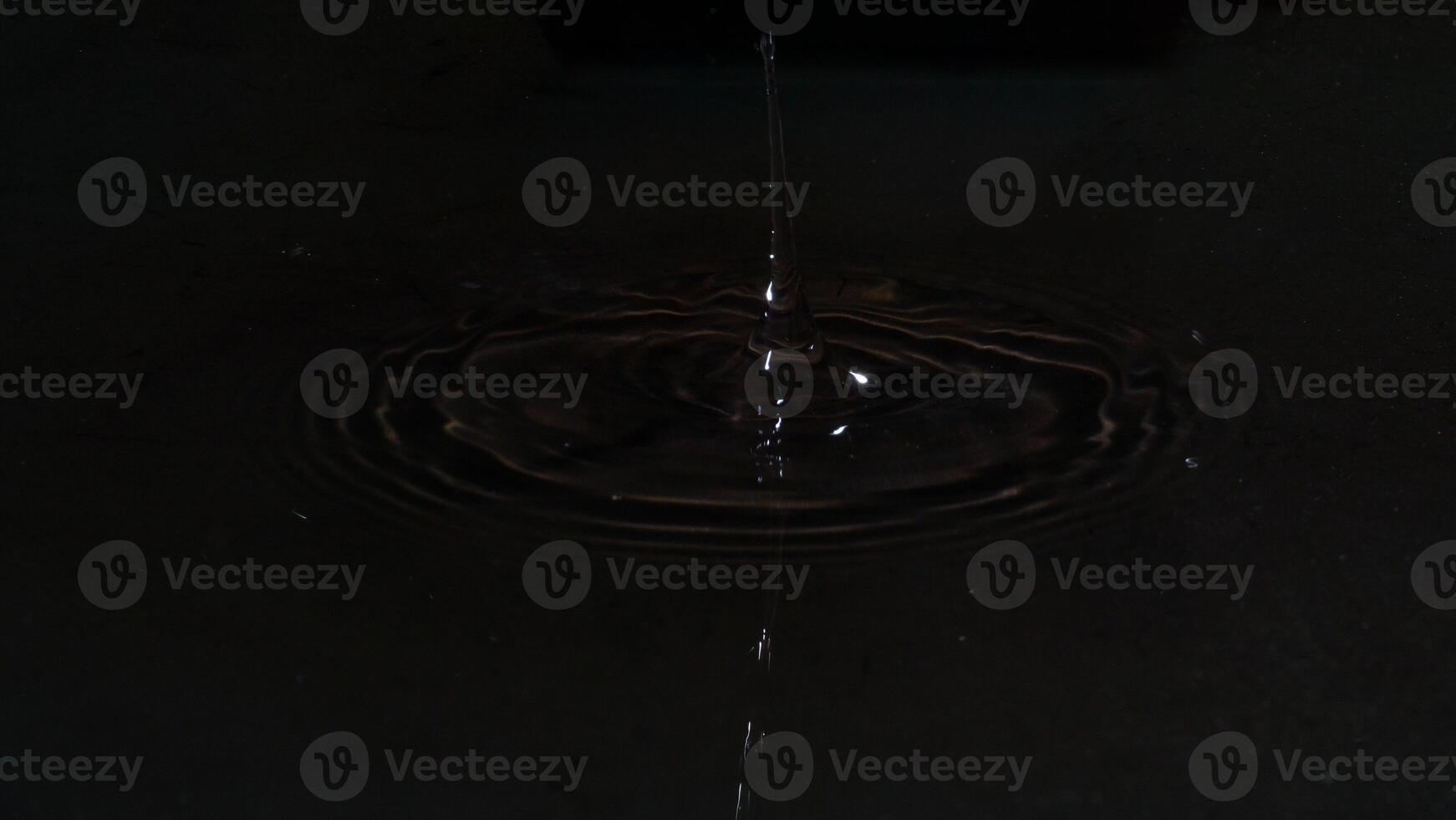 Drops of water on the water surface spreading and forming waves isolated on black background photo