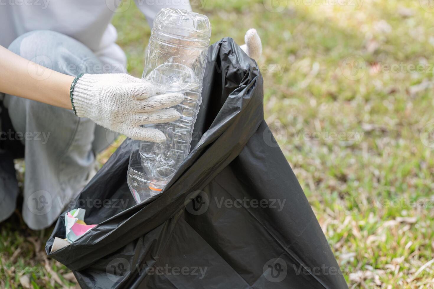 Individual collecting plastic bottles for recycling during a cleanup event in a park photo