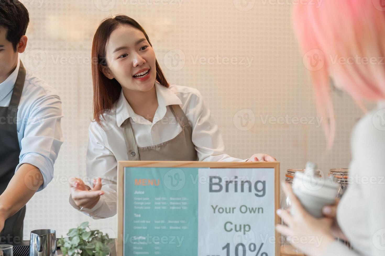 Sustainability and Customer Engagement. A barista explains the benefits of bringing a personal cup to a customer at a trendy cafe. photo