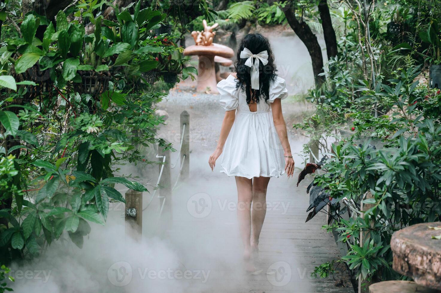 A fantasy elf woman in a white dress strolling through a fairy-tale forest with thick fog. photo