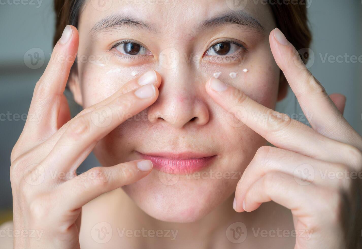 Asian woman applying anti aging cream on her under eyes. The anti aging cream is using to reducing, masking or preventing signs of skin aging. photo