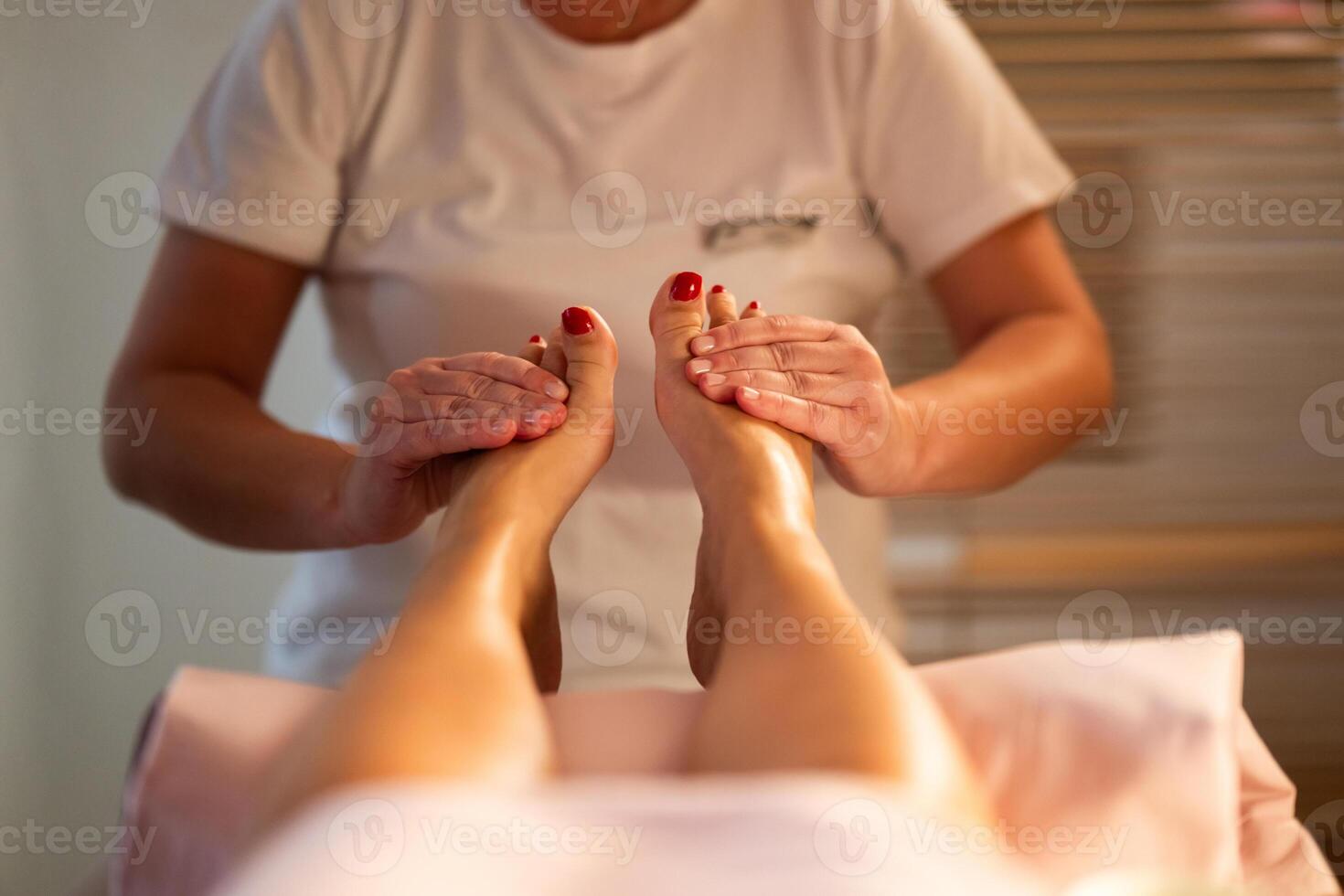 Foot Massage Therapy in a Relaxing Spa Setting. A professional massage therapist in a white uniform provides a soothing foot massage to a client in a calm and serene spa environment photo