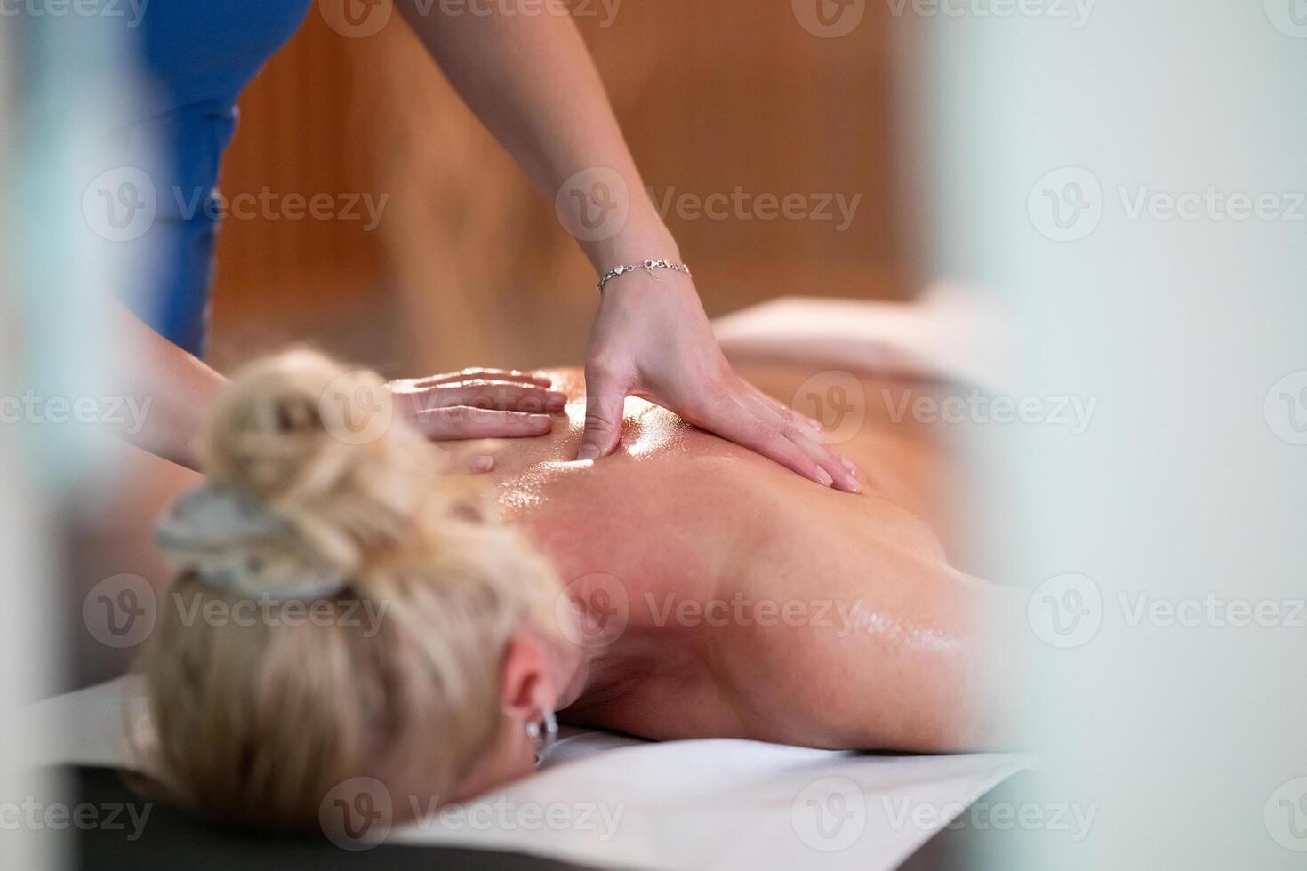 Relaxing Back Massage in a Spa Setting. A professional massage therapist in a blue uniform provides a relaxing back massage to a client lying on a massage table. photo