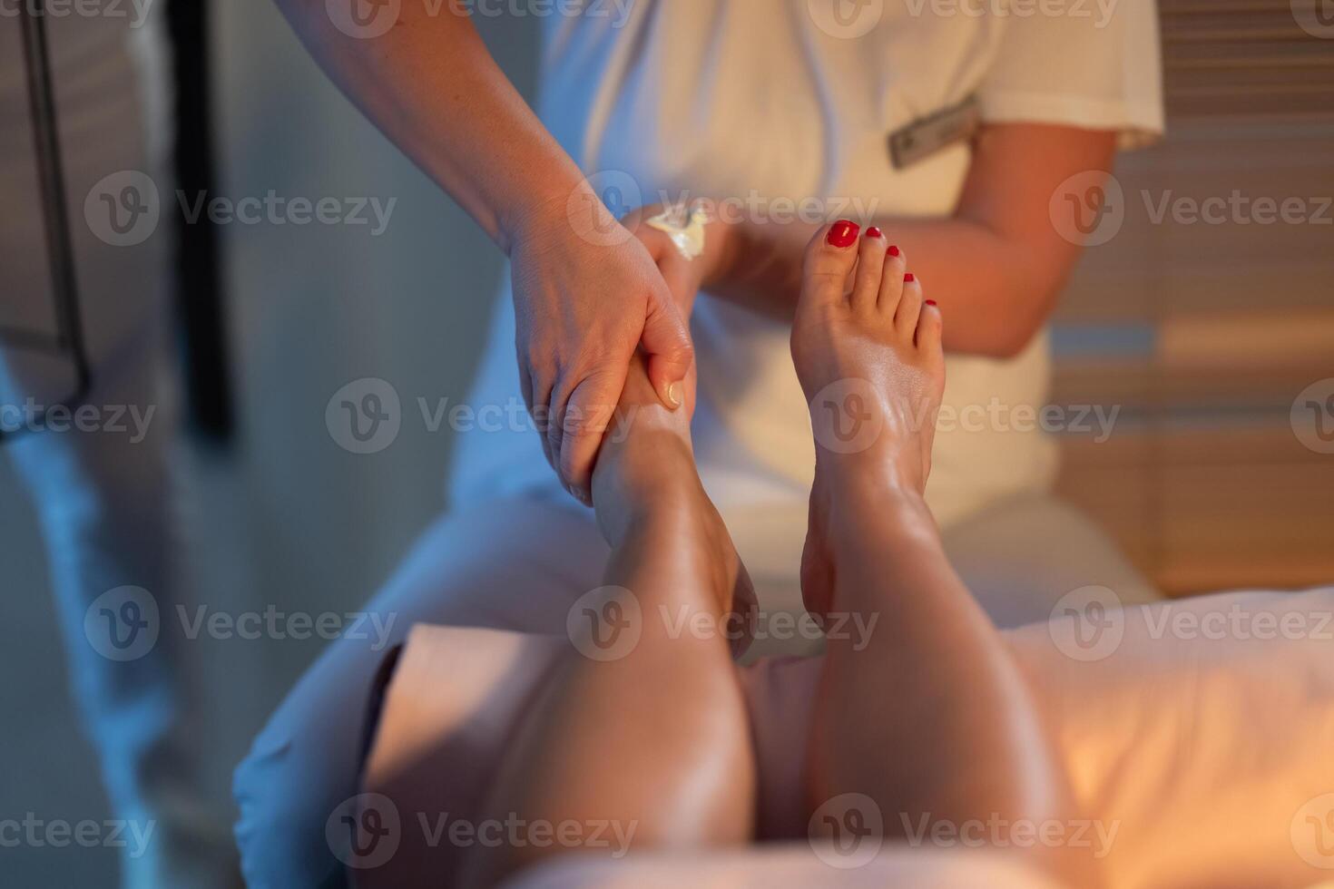 Foot Massage Therapy in a Relaxing Spa Setting. A professional massage therapist in a white uniform provides a soothing foot massage to a client in a calm and serene spa environment photo