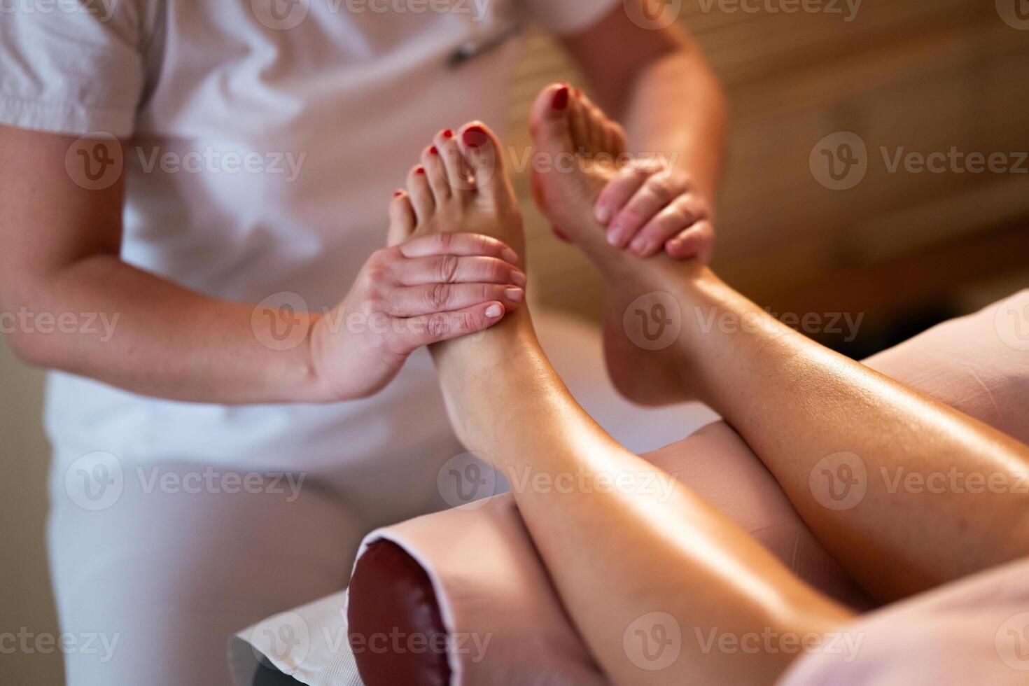 Foot Massage Therapy in a Relaxing Spa Setting. A professional massage therapist in a white uniform provides a soothing foot massage to a client in a calm and serene spa environment photo