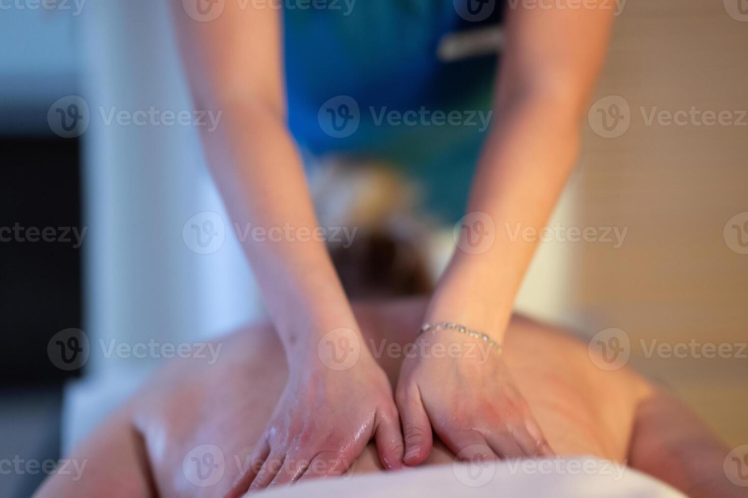 Relaxing Back Massage in a Spa Setting. A professional massage therapist in a blue uniform provides a relaxing back massage to a client lying on a massage table. photo