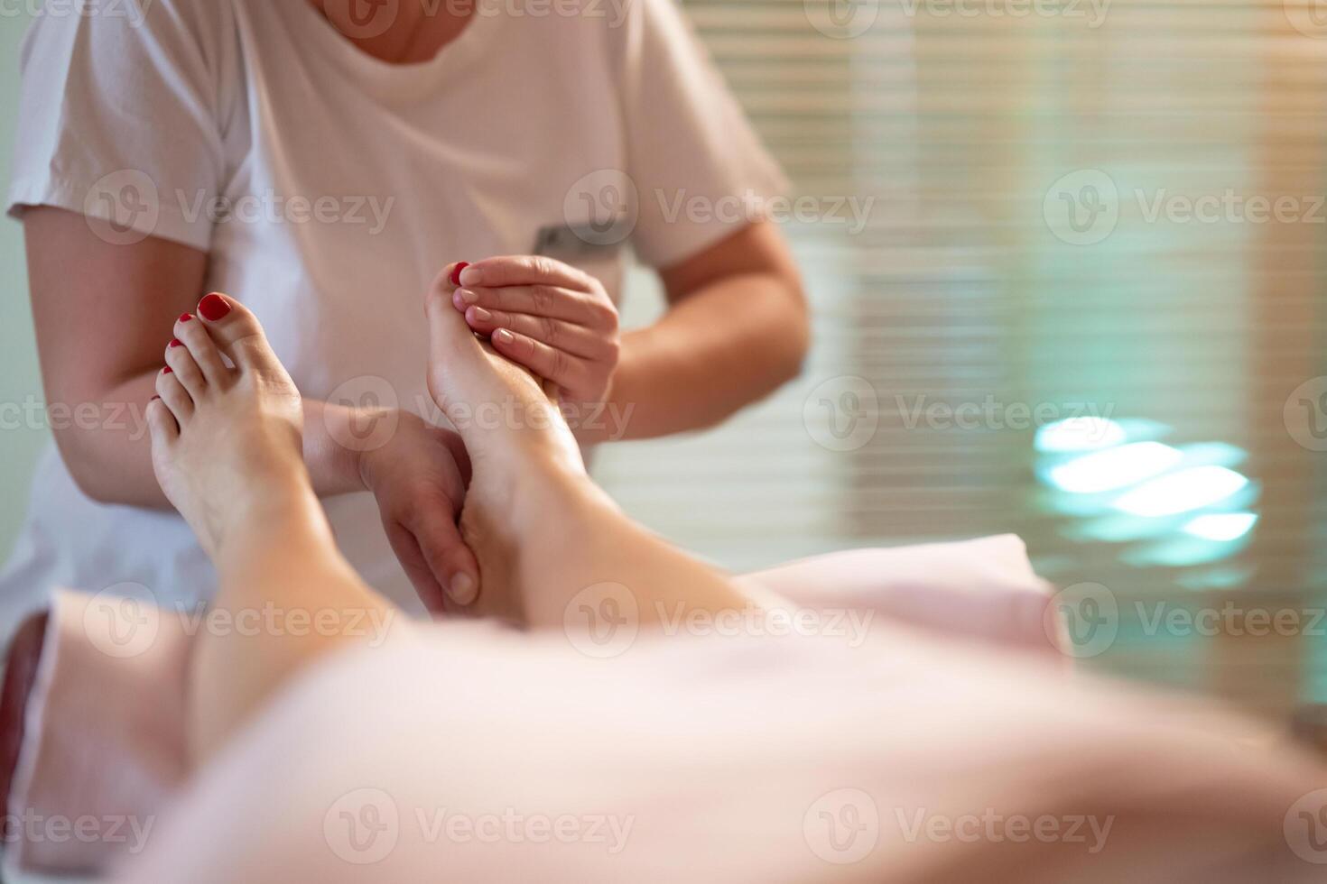 Foot Massage Therapy in a Relaxing Spa Setting. A professional massage therapist in a white uniform provides a soothing foot massage to a client in a calm and serene spa environment photo
