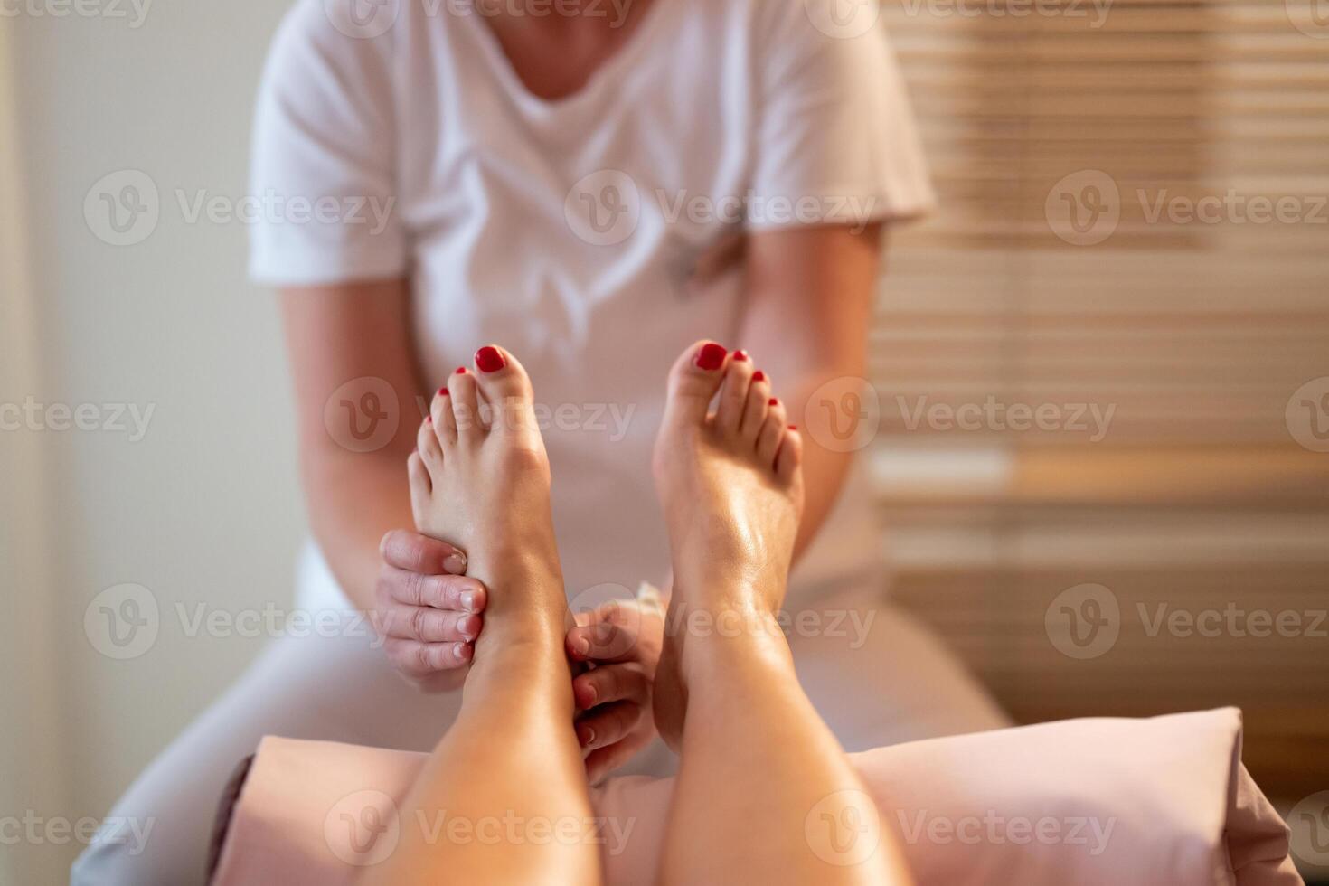 Foot Massage Therapy in a Relaxing Spa Setting. A professional massage therapist in a white uniform provides a soothing foot massage to a client in a calm and serene spa environment photo