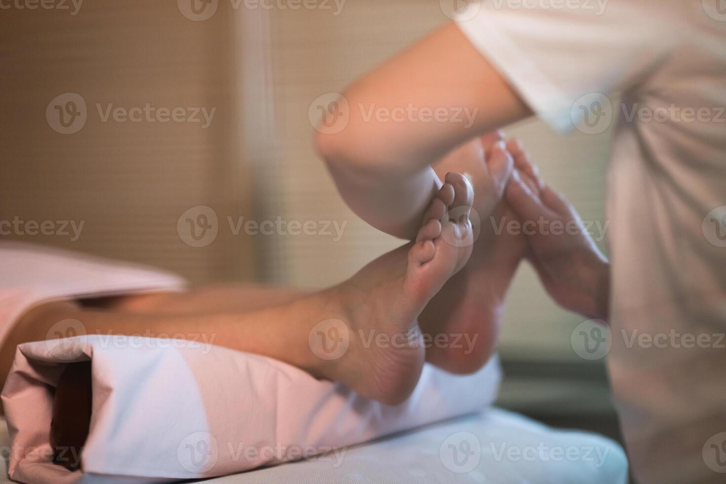 Foot Massage Therapy in a Relaxing Spa Setting. A professional massage therapist in a white uniform provides a soothing foot massage to a client in a calm and serene spa environment photo