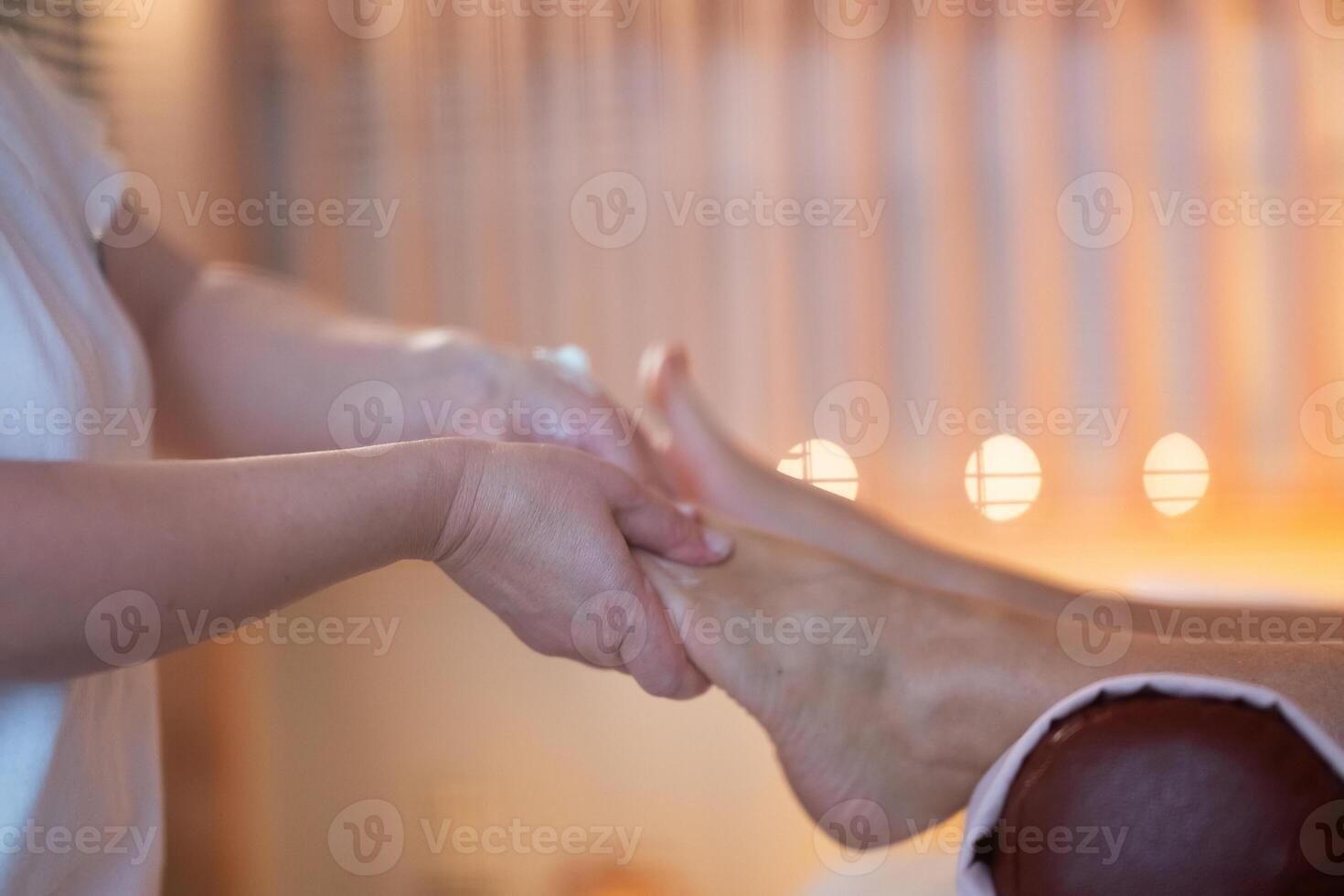 Foot Massage Therapy in a Relaxing Spa Setting. A professional massage therapist in a white uniform provides a soothing foot massage to a client in a calm and serene spa environment photo