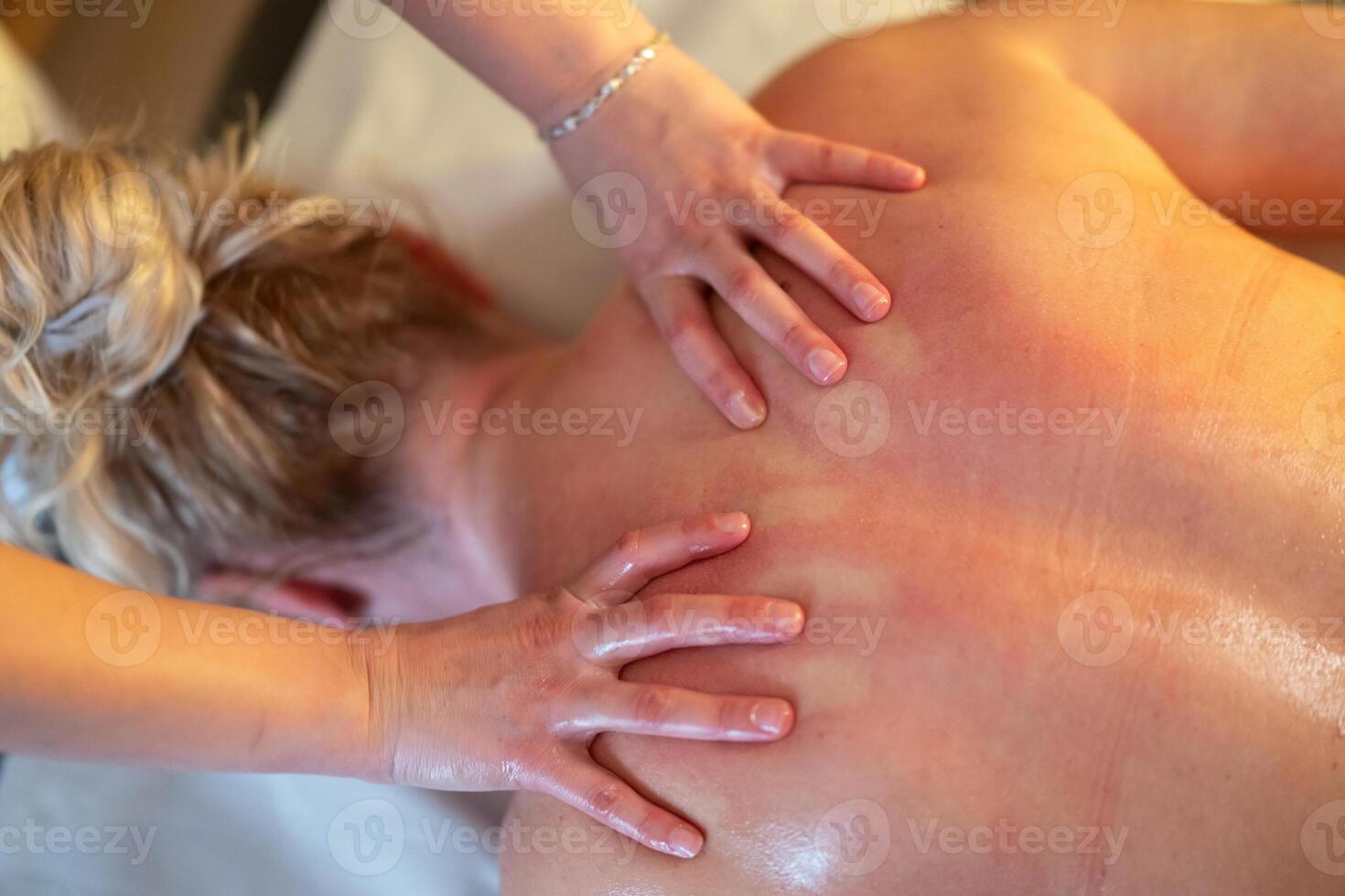 Relaxing Back Massage in a Spa Setting. A professional massage therapist in a blue uniform provides a relaxing back massage to a client lying on a massage table. photo