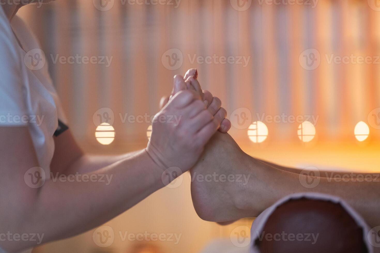 Foot Massage Therapy in a Relaxing Spa Setting. A professional massage therapist in a white uniform provides a soothing foot massage to a client in a calm and serene spa environment photo