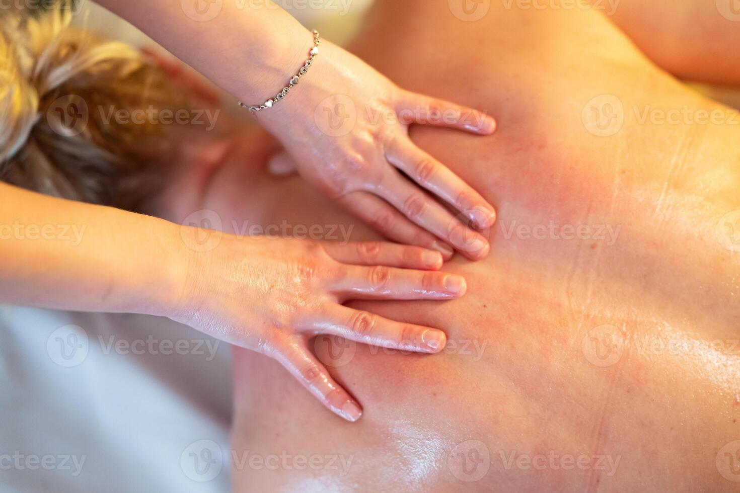 Relaxing Back Massage in a Spa Setting. A professional massage therapist in a blue uniform provides a relaxing back massage to a client lying on a massage table. photo