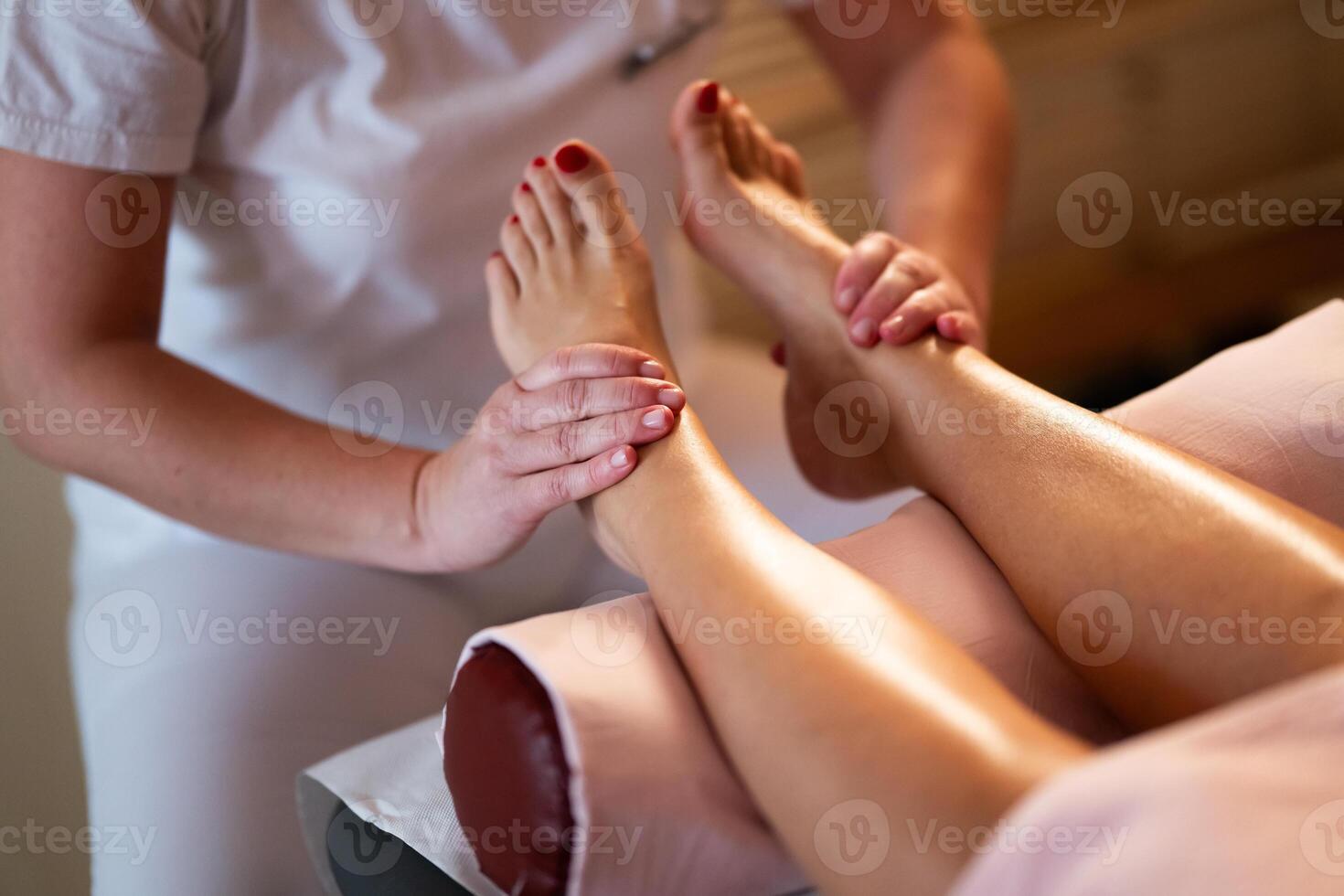 Foot Massage Therapy in a Relaxing Spa Setting. A professional massage therapist in a white uniform provides a soothing foot massage to a client in a calm and serene spa environment photo